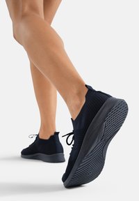 Baskets de sport tricotées bleu marine avec semelles en caoutchouc noir, dotées d'un système de laçage et d'un design texturé sur le dessus pour une meilleure respirabilité.