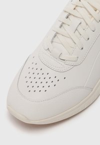 Light gray sneaker featuring a textured leather upper, perforated toe box, flat laces, and a rubber sole with subtle tread pattern.