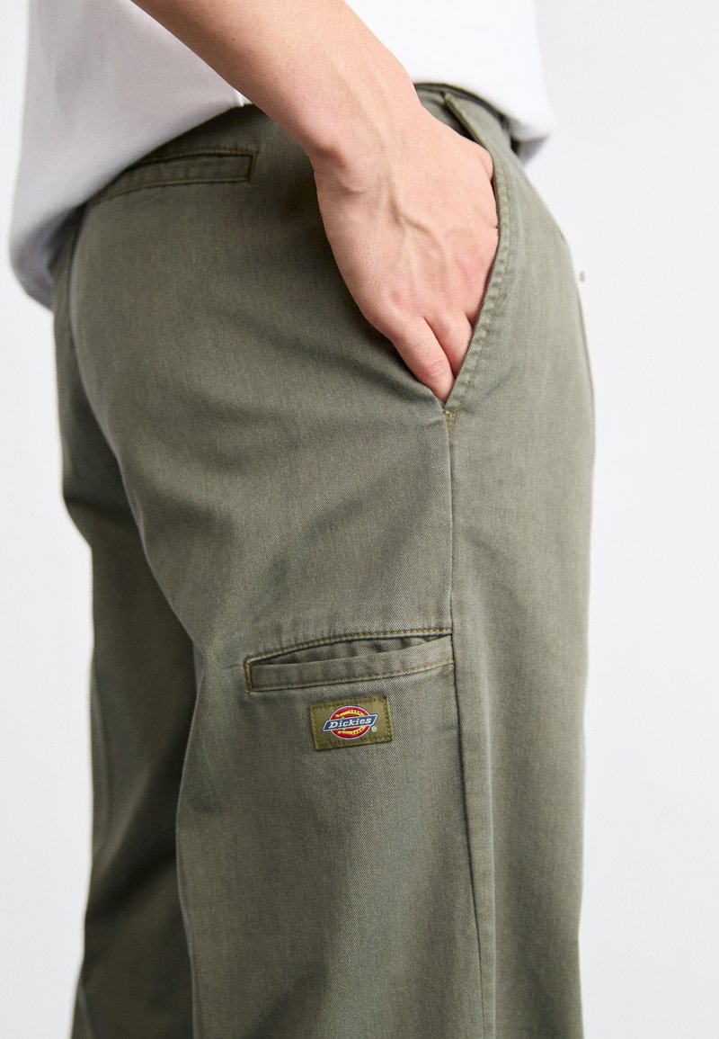 Grüne Baumwollhose mit einer Seitentasche, die ein rechteckiges, gesticktes Logo-Patch in Rot, Gelb und Grün am rechten Bein aufweist.