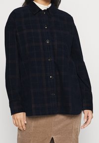 Giacca a camicia a quadri blu navy in morbido tessuto, con chiusura a bottoni, colletto a punta e righe bordeaux a contrasto nel motivo a quadri.