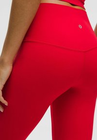 Primer plano de una persona que lleva leggings de cintura alta de color rojo brillante con costuras visibles y un pequeño logo en la parte posterior de la cinturilla.