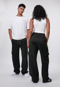 Unisex witte oversized t-shirt en zwarte wijde cargobroek met zakken, weergegeven van voren en van achteren. Zachte stof, relaxte pasvorm.
