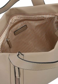 Sac fourre-tout en cuir beige avec une poche zippée et une doublure rayée orange et crème. Il présente des poignées robustes et un design structuré.