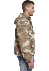 Veste de camouflage dans des tons beige et vert. Dotée d'une fermeture éclair, d'une capuche à cordons et de poches zippées sur les côtés. Tissu léger.