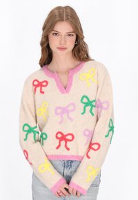Beige gestrickter Pullover mit V-Ausschnitt, der bunte Stickereibögen in Rot, Gelb, Pink und Grün zeigt. Rosafarbene Besätze am Hals und an den Bündchen.