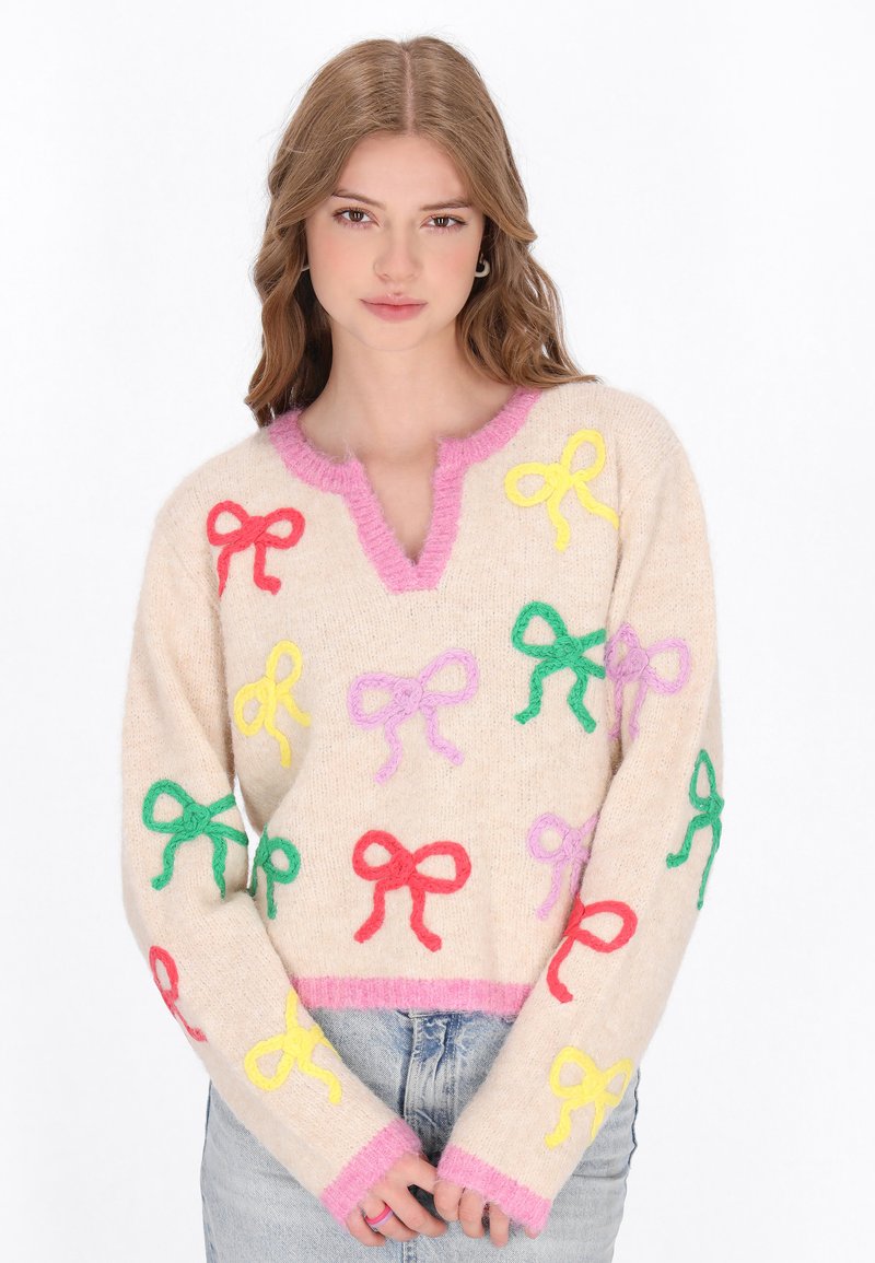 Beige gestrickter Pullover mit V-Ausschnitt, der bunte Stickereibögen in Rot, Gelb, Pink und Grün zeigt. Rosafarbene Besätze am Hals und an den Bündchen.
