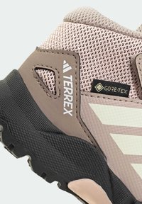 Zapatilla de trail de color rosa claro con parte superior de malla, detalles en gris y negro, suela de goma texturizada y detalle de logotipo en relieve. Cuenta con la marca GORE-TEX.