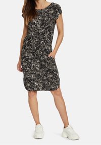 Svart klänning med vitt bladmönster, korta ärmar, rund hals, och fickor, tillverkad av mjukt tyg, som slutar ovanför knäna.