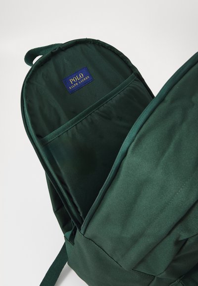 Mochila de color verde oscuro con una textura de tela suave, que cuenta con un bolsillo frontal y una etiqueta azul con "POLO RALPH LAUREN" en el interior.