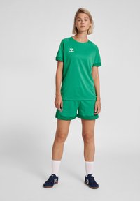 Grön sportklädsel som består av en kortärmad tröja och matchande shorts, tillverkade av ett andningsbart material, med logotypdetaljer och kontrasterande sömmar.