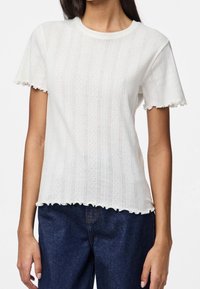 Vit kortärmad topp med strukturerade ränder, rund halsringning och volangkant vid nederkant och ärmar. Tyget verkar lätt och luftigt.