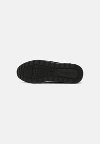 Semelle de chaussure en caoutchouc noir avec un motif de grip texturé et un logo. Présente des rainures profondes pour une adhérence et un design plat et robuste.