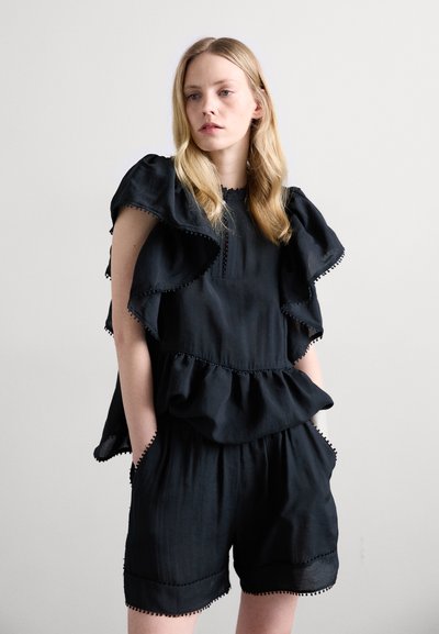 Melna ruffles top ar slāņu dizainu, ar īsām piedurknēm un teksturētu apdari, pārī ar atbilstošām šortiem, akcentētiem ar pom-pom apdari.