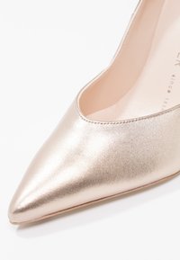 Escarpin pour femme en beige métallisé à bout pointu, avec une texture en cuir lisse et des coutures subtiles le long du bord, présenté en gros plan.