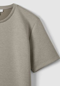 Tricou cu mânecă scurtă, gât rotund, dintr-un material moale, gri deschis. Prezintă o croială lejeră, cu o textură netedă și detalii de cusătură minime.