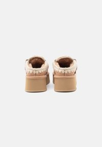 Faux fur gevoerde instappers met een beige suède bovenkant, ronde achterkant, geweven detail langs de rand en een lichtbruine dikke zool.
