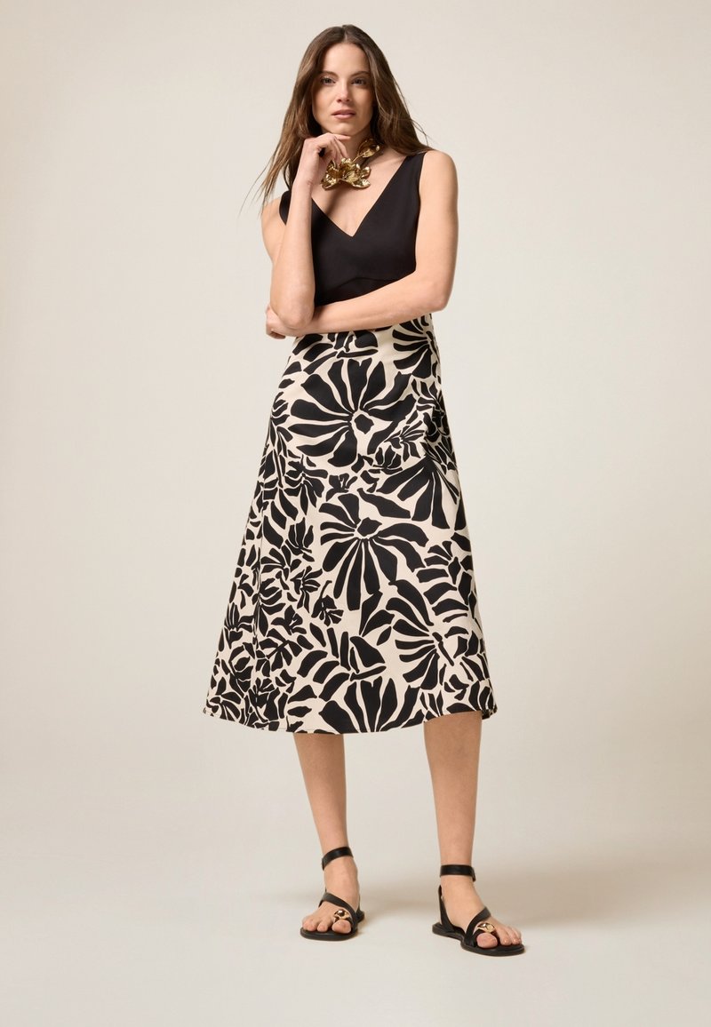 Midikleid mit beigem Hintergrund und kräftigen schwarzen Blumenmustern, kombiniert mit einem ärmellosen schwarzen Oberteil und einfachen schwarzen Sandalen.