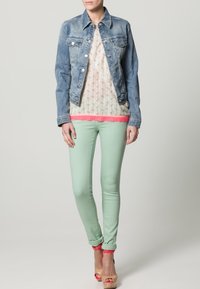 Ljusblå denimjacka över en blommönstrad blus med rosa kant, matchad med mintgrön slim-fit jeans och tan hixtsandaler med rosa accenter.