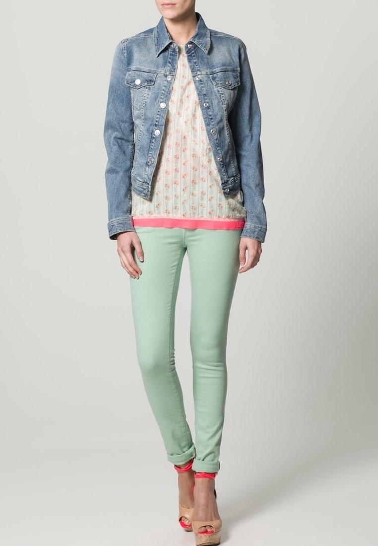 Ljusblå denimjacka över en blommönstrad blus med rosa kant, matchad med mintgrön slim-fit jeans och tan hixtsandaler med rosa accenter.