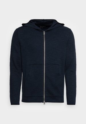 Granatowy hoodie na zamek, wykonany z teksturowanej tkaniny, z przednią kieszenią i kapturem ze sznurkiem. Posiada srebrny zamek i ściągacze przy rękawach.