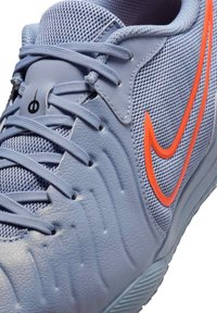 Világoskék sportcipő, hálós és szintetikus bőrből készült, narancssárga Nike logóval, textúrázott részletekkel és fűzős záródással.