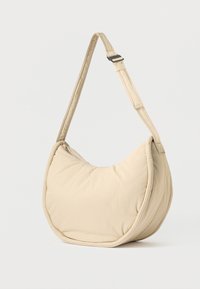 Μπεζ τσάντα ώμου με επένδυση, καμπυλωτή σιλουέτα, ρυθμιζόμενο λουρί και λείο υφασμάτινο υλικό. Διαθέτει φερμουάρ στο πάνω μέρος.