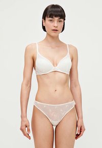 White lingerie set featuring a triangular cup bra with floral texture and thin straps, paired with sheer floral-embroidered briefs.