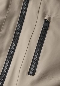 Tissu beige à texture lisse comportant deux fermetures éclair noires, l'une avec un curseur et l'autre avec une bande décorative. Détails de couture visibles.