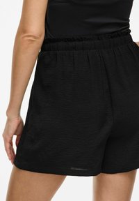 Pantaloni shorts neri realizzati in tessuto stropicciato con vita elastica. L'orlo è leggermente sopra il ginocchio, mettendo in risalto una vestibilità comoda.