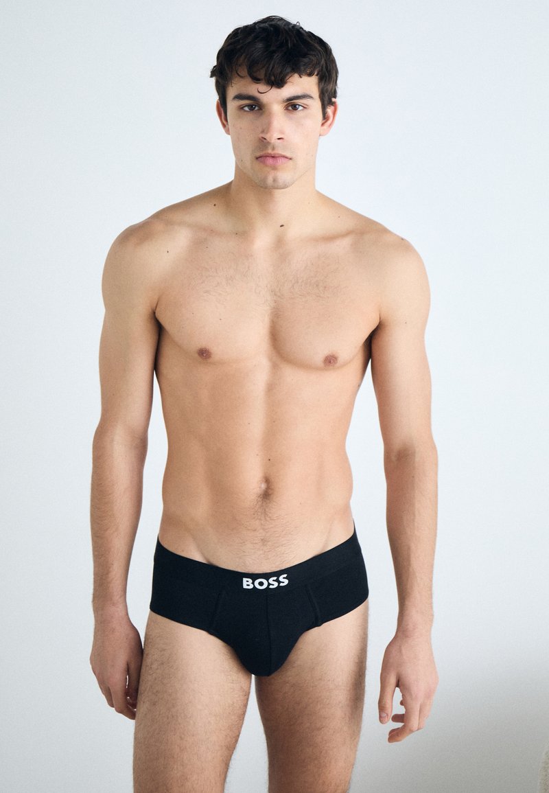 Slip da uomo neri in cotone con logo "BOSS" bianco sulla cintura; il modello assume una postura neutra, lo sfondo è semplice e chiaro.
