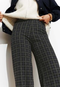 Pantalons larges à carreaux gris foncé, présentant un motif à carreaux avec des accents bleus. Texture douce, associés à un pull en maille crème.
