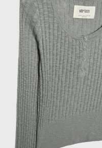 Pull en maille côtelée gris avec encolure dégagée, quatre petits boutons au centre devant et une étiquette de marque indiquant "str teen" à l'intérieur du col.