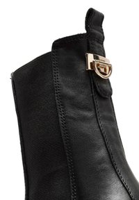 Black ankle boot featuring a smooth leather upper, elastic side panels, and a gold-tone buckle accent on the outer side.