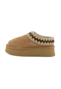 Scarpe slip-on in suede marrone con un colletto intrecciato in crema e marrone scuro dalla texture, dotate di una suola piatta spessa e una parte inferiore in gomma.