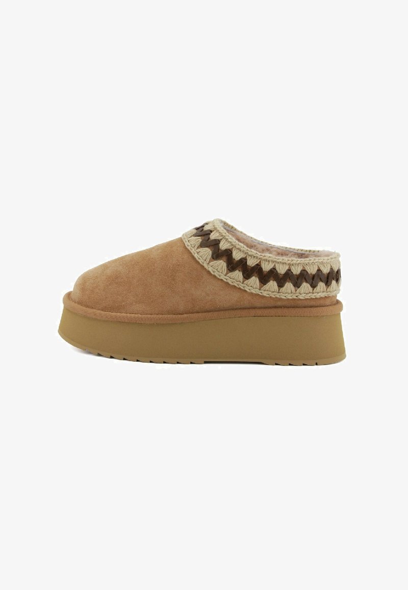 Scarpe slip-on in suede marrone con un colletto intrecciato in crema e marrone scuro dalla texture, dotate di una suola piatta spessa e una parte inferiore in gomma.
