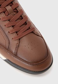 Baskets en cuir marron avec surface texturée, bout arrondi et perforations respirantes. Équipées de lacets plats et tressés et d'une semelle en caoutchouc contrastante.