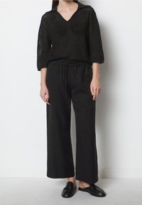 Schwarzes, locker sitzendes, kurz geschnittenes Top mit V-Ausschnitt und 3/4-Ärmeln, kombiniert mit weit geschnittenen schwarzen Hosen und schwarzem Slip-On-Schuhen.