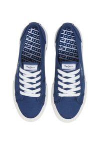 Modri platneni športni copati z belimi vezalkami in gumijastimi podplati. Na ježku je prikazana oznaka, podlage pa so vzorčaste z ponavljajočim se besedilom.