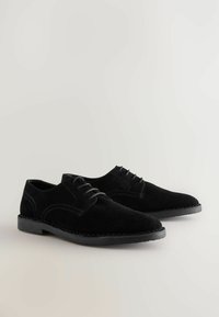 Zapatos de ante negros con cordones, de textura suave, puntera redonda y un sencillo detalle de costura en los laterales. Suelas de goma negra.