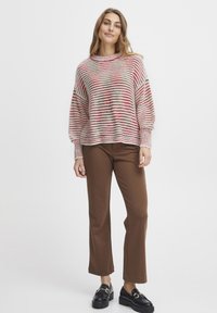 Stickad tröja med horisontella röda och grå ränder, rund hals, och långa ärmar, i kombination med bruna vida byxor och svarta loafers.