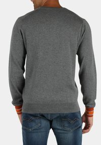 Maglione grigio con maniche lunghe, polsini a coste con strisce arancioni e un design aderente, indossato con jeans blu.