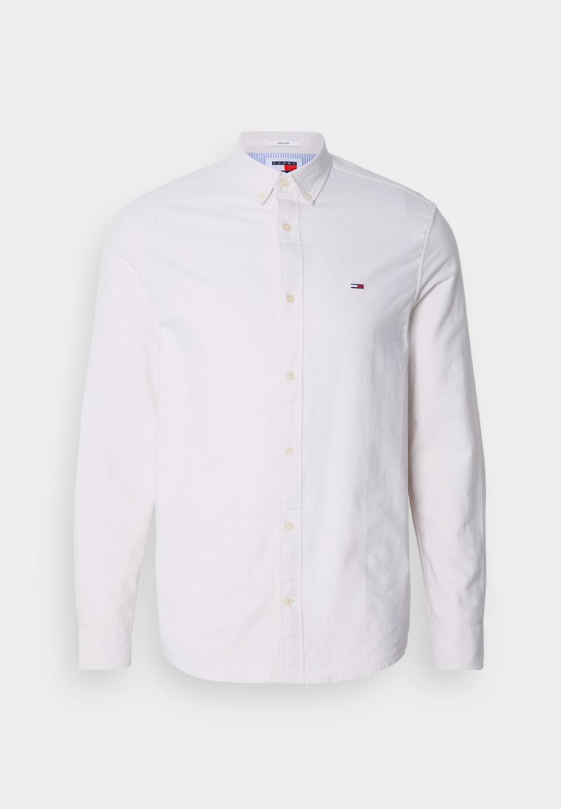 Camisa blanca de botones en tejido de algodón, con cuello alzado, mangas largas y un pequeño acento de logo en rojo, azul y blanco en el pecho.