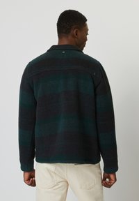 Chaqueta de mezcla de lana para hombre con rayas en verde oscuro y azul marino, con cuello puntiagudo y cierre de botones. Textura suave, ajuste casual.