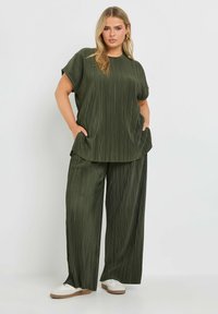 Olivgrön tvådelad set med en plisserad topp med korta ärmar och vida byxor. Mjuk tyg med synlig textur och fickor.