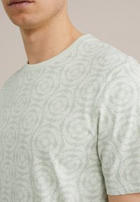 Camiseta de manga corta verde claro con un estampado floral y una textura suave, con cuello redondo y diseño de corte holgado.