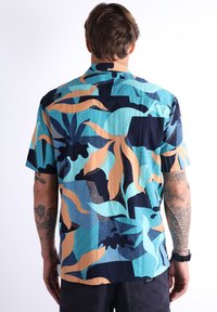 Chemise à manches courtes avec un motif tropical abstrait coloré dans des tons de bleu canard, marine et beige. Fabriquée en tissu léger avec une finition texturée.