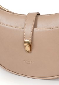 Beige leren handtas met een gebogen vorm, gouden sluiting en geperst logo. Gladde textuur met contrasterende stiksels.