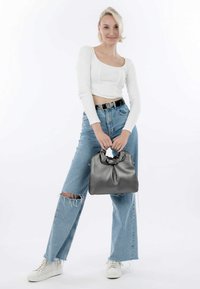 Borsa a mano in pelle grigia con manico arricciato, texture morbida e forma strutturata, abbinata a jeans chiari strappati e sneakers bianche.