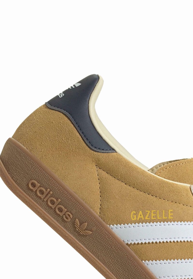 Wildleder Sneaker in Senfgelb mit weißen und grauen Streifen, ausgestattet mit einer tanfarbigen Gummisohle, goldenen "GAZELLE"-Buchstaben und einem glatten Lederakzent.