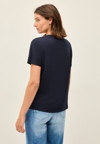 T-shirt à manches courtes bleu marine en tissu doux, avec une coupe décontractée et un col rond. Porté avec un jean léger bleu clair à coupe ample.